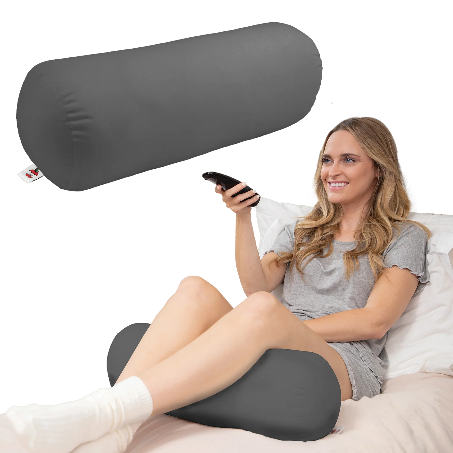 Woman relaxing in bed using a gray neck roll pillow under her legs while sitting and watching TV