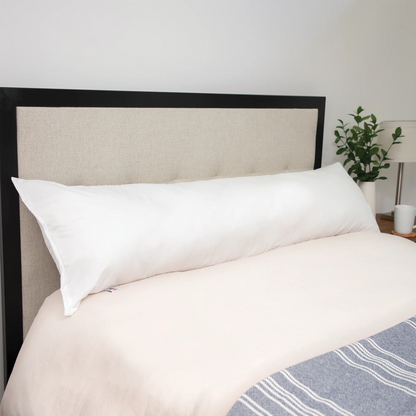 Long white body pillow placed across a neatly made bed with a beige headboard.