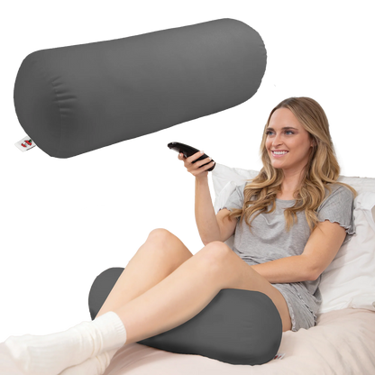 Woman relaxing in bed using a gray neck roll pillow under her legs while sitting and watching TV